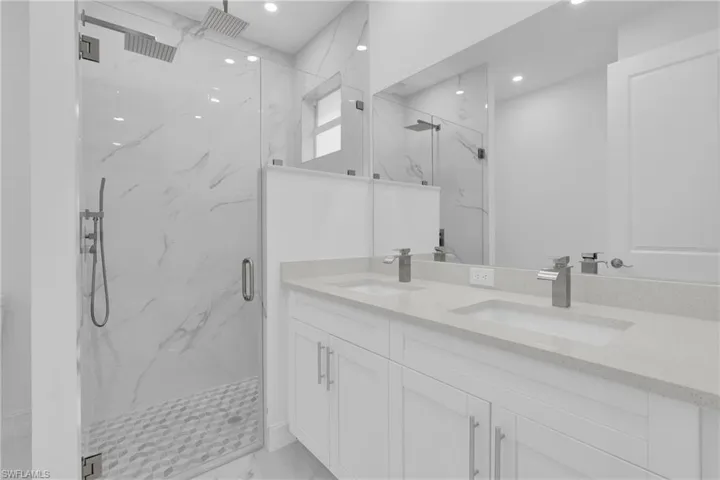 Full bathroom featuring a marble finish shower, double vanity, recessed lighting, and light marble finish floors