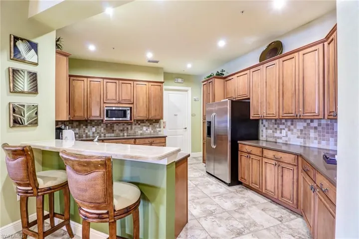 Kitchen with brown cabinetry, a kitchen bar, a peninsula, stainless steel appliances, and recessed lighting