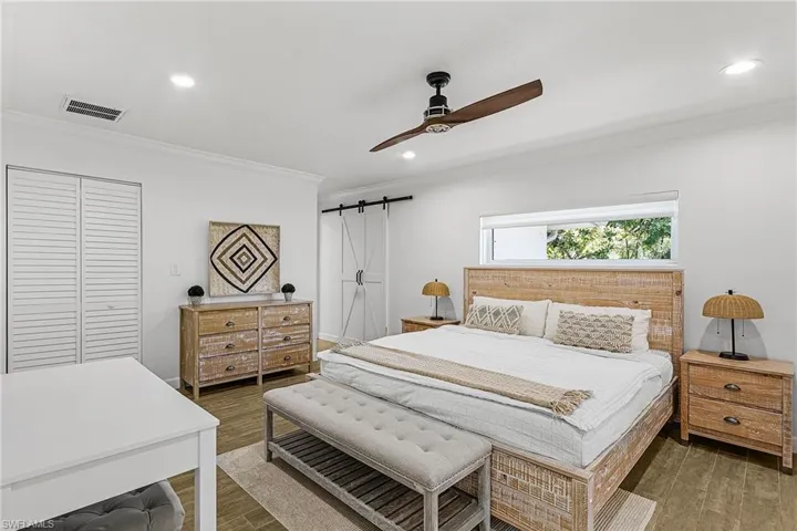 Bedroom with a closet, a barn door, crown molding, wood finished floors, and a ceiling fan