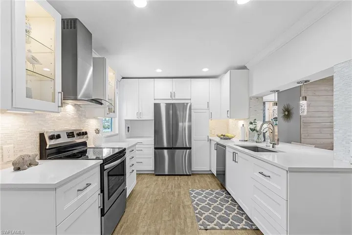 Kitchen featuring stainless steel appliances, wall chimney exhaust hood, glass insert cabinets, white cabinets, and light stone countertops