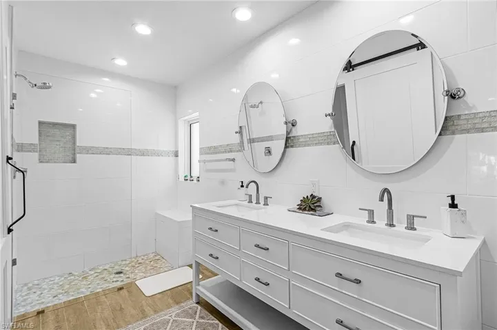 Full bath featuring walk in shower, double vanity, tile walls, recessed lighting, and light wood-style flooring