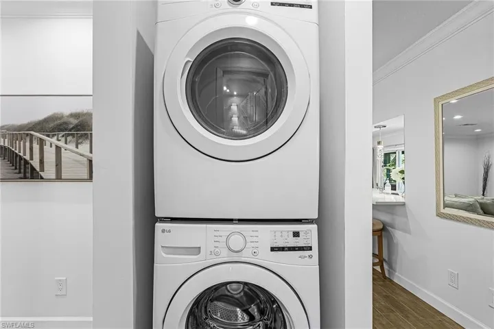 Laundry area featuring ornamental molding, wood finished floors, and estacked washer and dryer