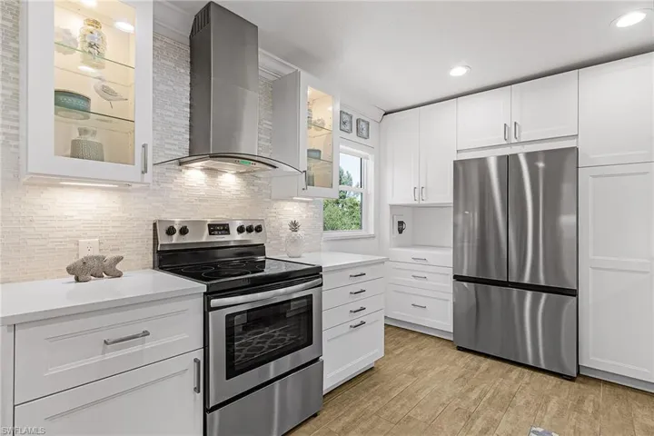 Kitchen with stainless steel appliances, white cabinets, wall chimney range hood, glass insert cabinets, and light wood-type flooring