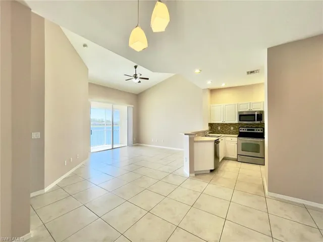Kitchen featuring decorative light fixtures, open floor plan, stainless steel appliances, a peninsula, and light tile patterned floors