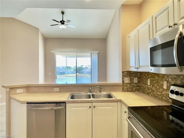 Kitchen featuring stainless steel appliances, light countertops, ceiling fan, white cabinetry, and a peninsula