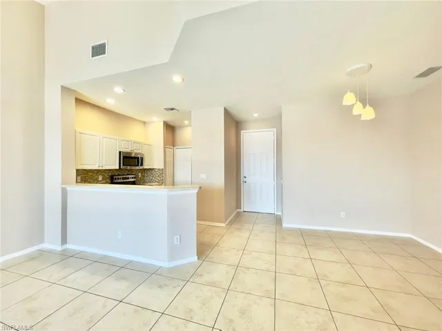Kitchen featuring decorative light fixtures, stainless steel microwave, light countertops, a peninsula, and white cabinets