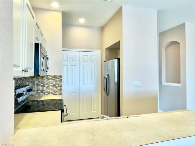 Kitchen with stainless steel appliances, white cabinets, decorative backsplash, and recessed lighting