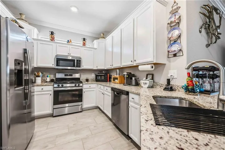 Kitchen with stainless steel appliances, white cabinets, light stone countertops, and ornamental molding
