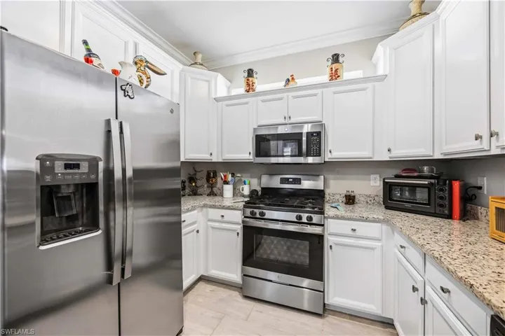 Kitchen featuring stainless steel appliances, white cabinetry, light stone counters, and ornamental molding