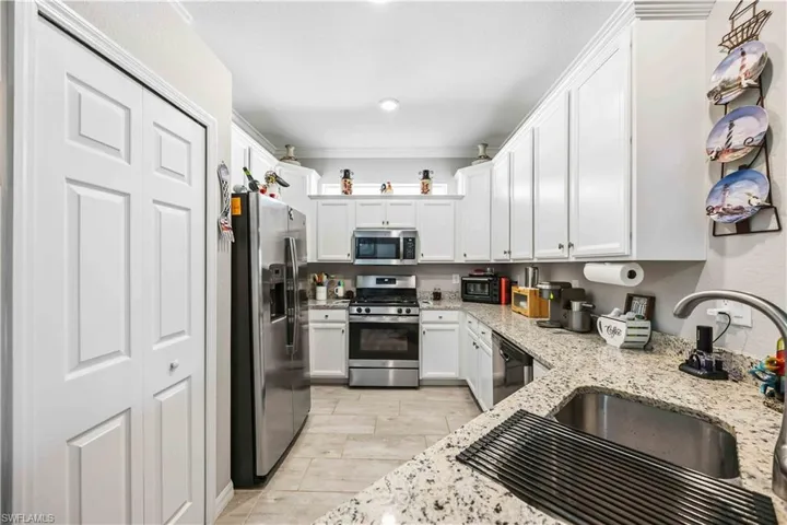 Kitchen featuring stainless steel appliances, ornamental molding, white cabinetry, and light stone countertops