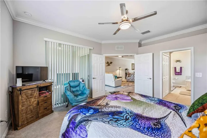 Bedroom featuring light colored carpet, ornamental molding, ensuite bathroom, and a ceiling fan