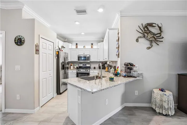 Kitchen featuring stainless steel appliances, ornamental molding, a peninsula, light stone counters, and white cabinets