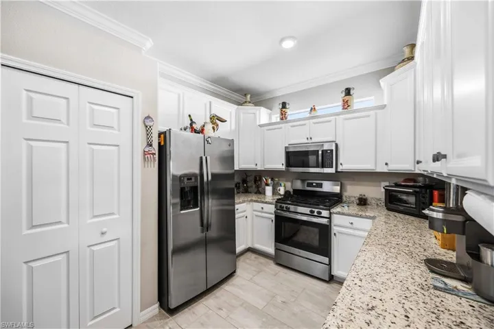 Kitchen featuring stainless steel appliances, crown molding, light stone countertops, white cabinetry, and light wood-type flooring