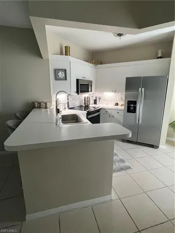 Kitchen featuring white cabinetry, stainless steel appliances, a white subway tile backsplash, and a breakfast bar with an integrated sink
