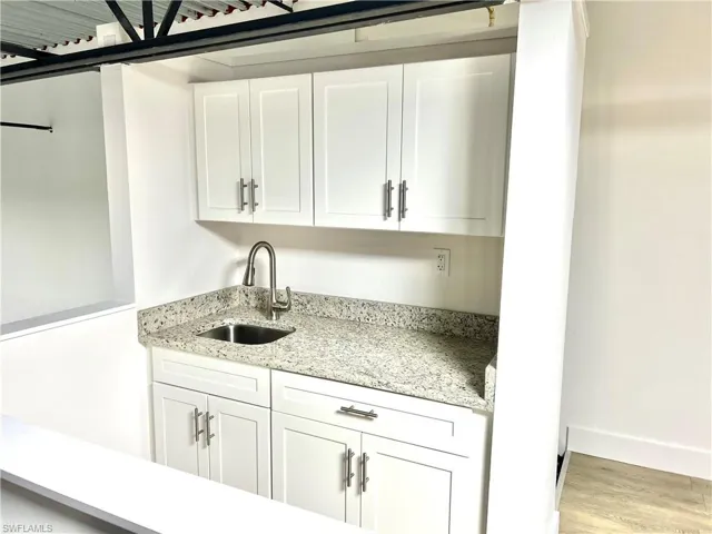 Kitchen featuring sink, light stone countertops, light hardwood / wood-style floors, and white cabinetry