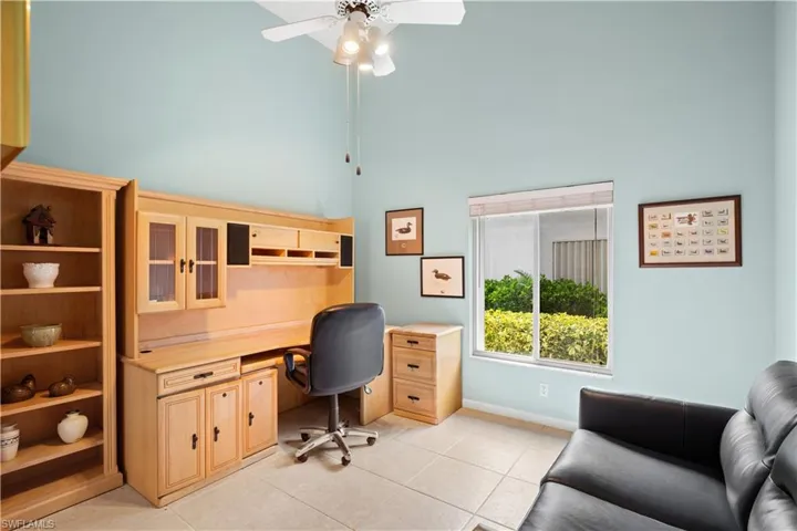 Vaulted ceiling with a ceiling fan, built-in light wood cabinetry, tile flooring, and a large window