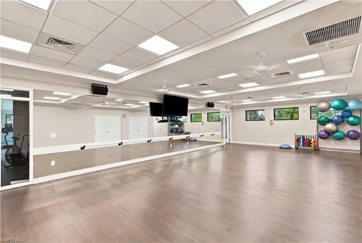 Wood-finish flooring, extensive wall-mounted mirrors, recessed lighting, ceiling fans, and multiple windows