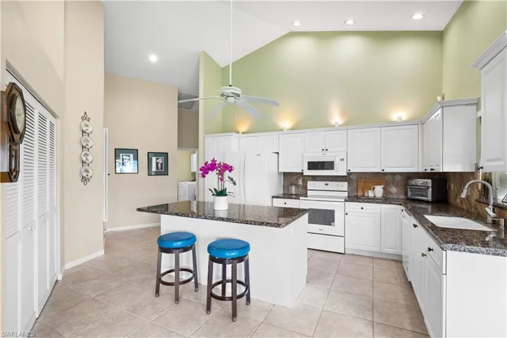 Kitchen featuring vaulted ceilings, white cabinetry, a center island with a stone countertop, and tile flooring