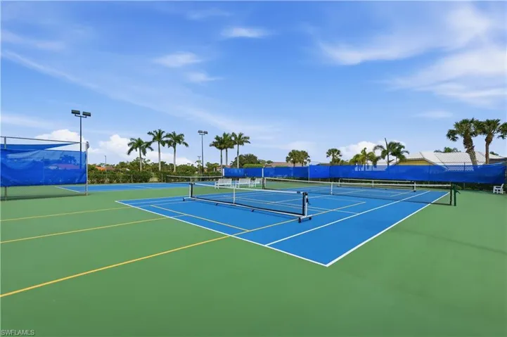 Tennis courts with blue and green surfaces, perimeter fencing, and mature palm trees