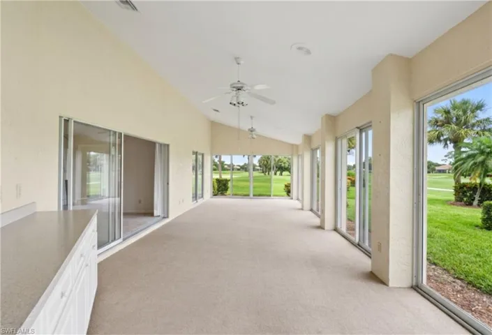 Spacious enclosed lanai featuring vaulted ceilings, multiple sliding glass doors, ceiling fans, and built-in cabinetry with a countertop