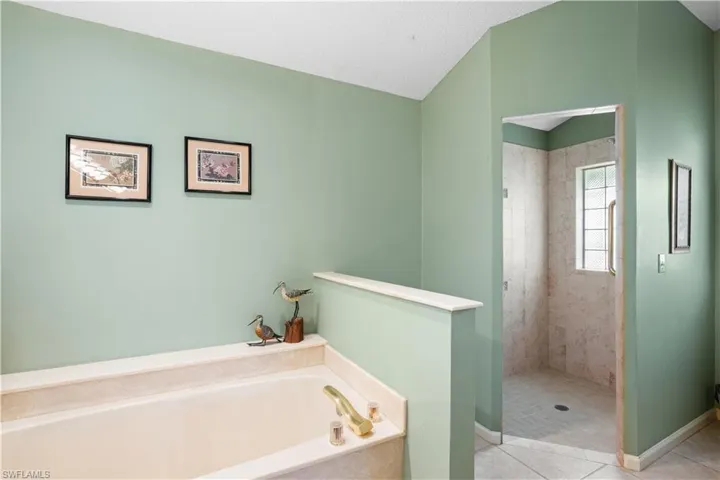 Built-in soaking tub with brass fixtures, tile surround, and a separate glass-enclosed shower featuring full-height tile walls and a grid-pattern window