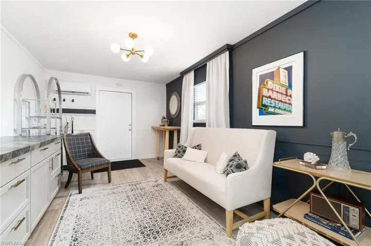 Living room featuring an inviting chandelier, an AC wall unit, light wood-type flooring, and crown molding