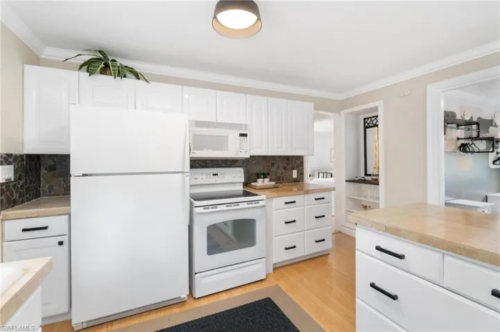 Kitchen with light hardwood / wood-style flooring, white appliances, tasteful backsplash, ornamental molding, and white cabinetry