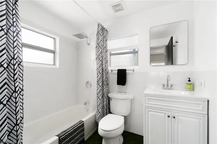 Full bathroom with toilet, vanity, shower / bath combo with shower curtain, and tile walls