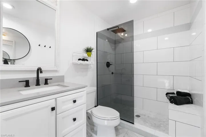 Bathroom featuring a shower with door, tile flooring, vanity with extensive cabinet space, and toilet