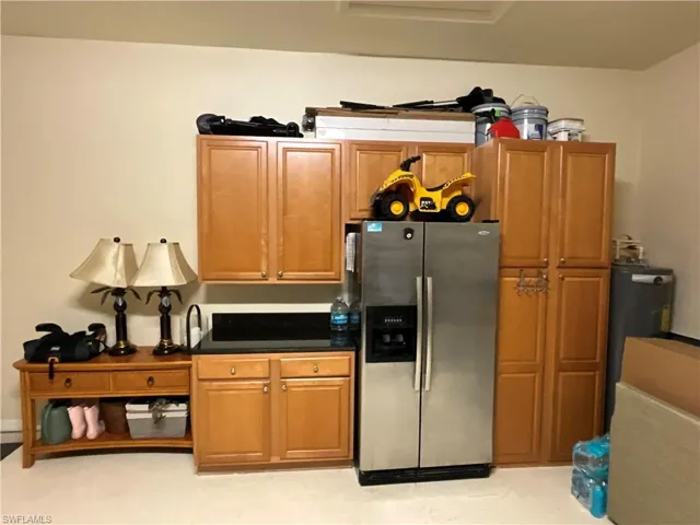 Kitchen with brown cabinetry, dark countertops, and stainless steel fridge