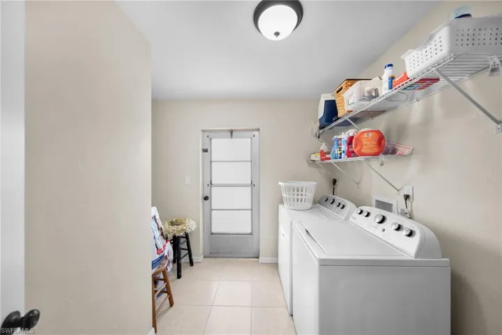 Washroom with washing machine and clothes dryer and light tile patterned flooring