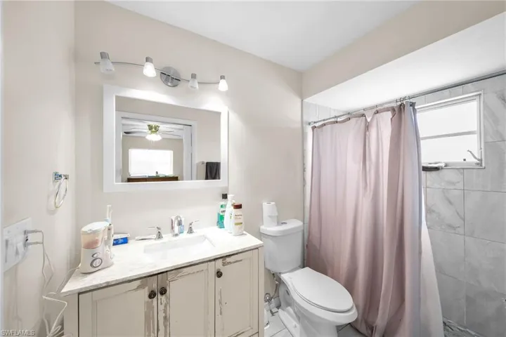 Bathroom with walk in shower, toilet, ceiling fan, and vanity