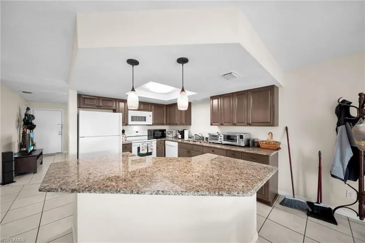Kitchen with hanging light fixtures, light tile patterned floors, white appliances, sink, and a kitchen island