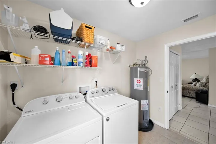Clothes washing area featuring light tile patterned floors, water heater, and washing machine and dryer