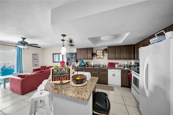Kitchen with white appliances, ceiling fan, hanging light fixtures, a raised ceiling, and light tile patterned flooring