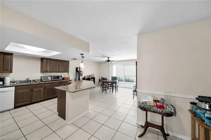 Kitchen featuring a raised ceiling, white dishwasher, hanging light fixtures, ceiling fan, and light stone counters