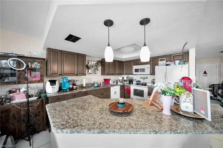 Kitchen featuring white appliances, light stone countertops, sink, dark brown cabinets, and pendant lighting