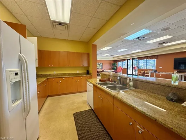 Kitchen with a sink, a drop ceiling, white appliances, and light floors