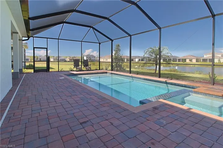 Screened enclosure featuring a swimming pool, integrated spa, and brick paver decking