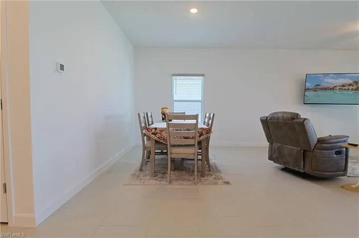 Recessed lighting illuminates the open-concept room featuring light-toned tile flooring, a window with blinds, and clean white walls