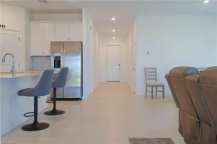 Recessed lighting illuminates the tiled flooring extending through the hallway