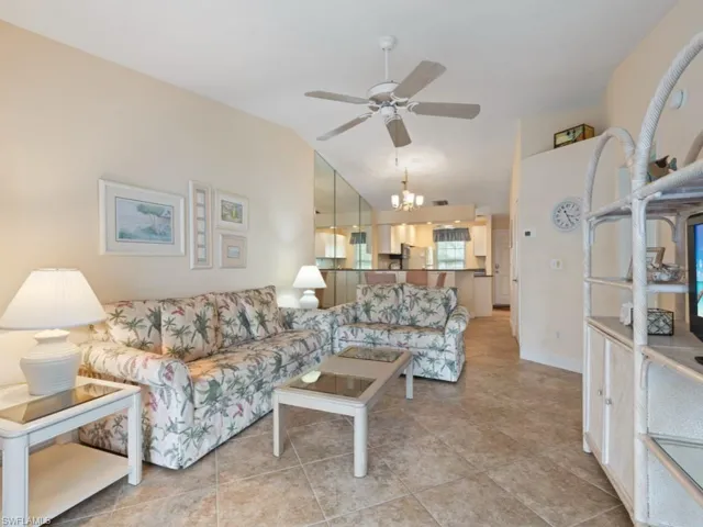 Living room with vaulted ceiling, ceiling fan with notable chandelier, and light tile patterned floors