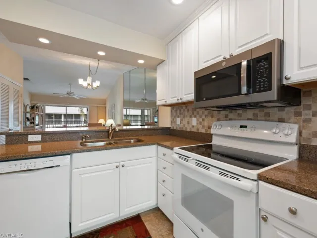 Kitchen with sink, white cabinetry, white appliances, ceiling fan with notable chandelier, and backsplash