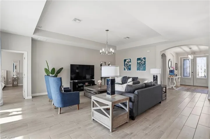 Living area featuring a raised ceiling, arched walkways, a chandelier, and wood tiled floors