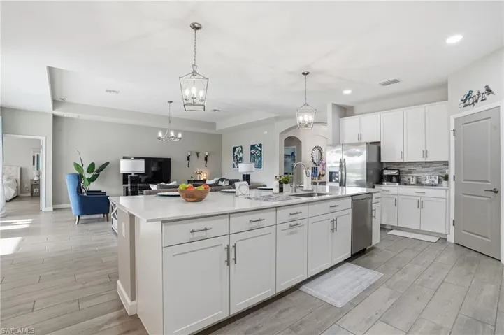 Kitchen with wood finish floors, white cabinetry, an island with sink, stainless steel appliances, and open floor plan
