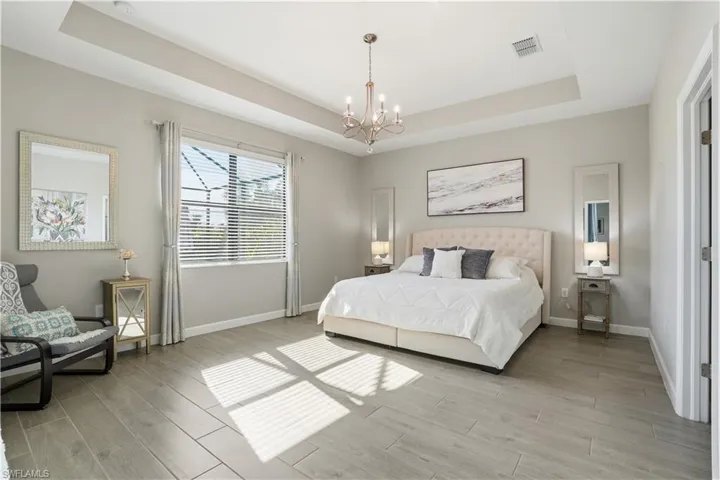 Bedroom featuring a raised ceiling, hanging lights, and wood finish floors