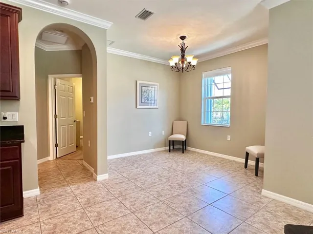 Unfurnished room with arched walkways, crown molding, light tile patterned floors, and a chandelier