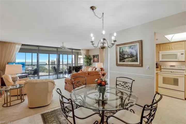 Dining room featuring a water view, a skylight, light tile patterned floors, expansive windows, and ceiling fan with notable chandelier