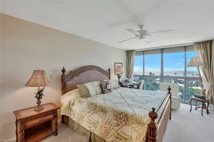 Bedroom with light carpet, expansive windows, ceiling fan, and a water view
