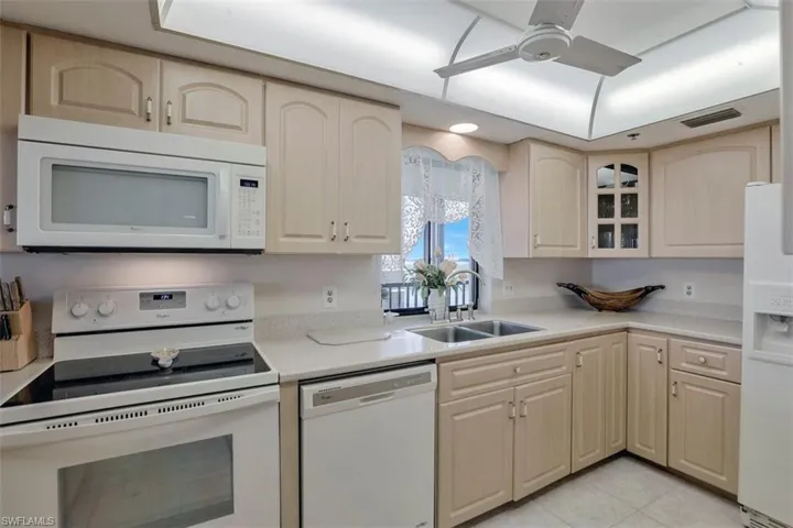 Kitchen with light brown cabinetry, sink, white appliances, light tile patterned floors, and ceiling fan